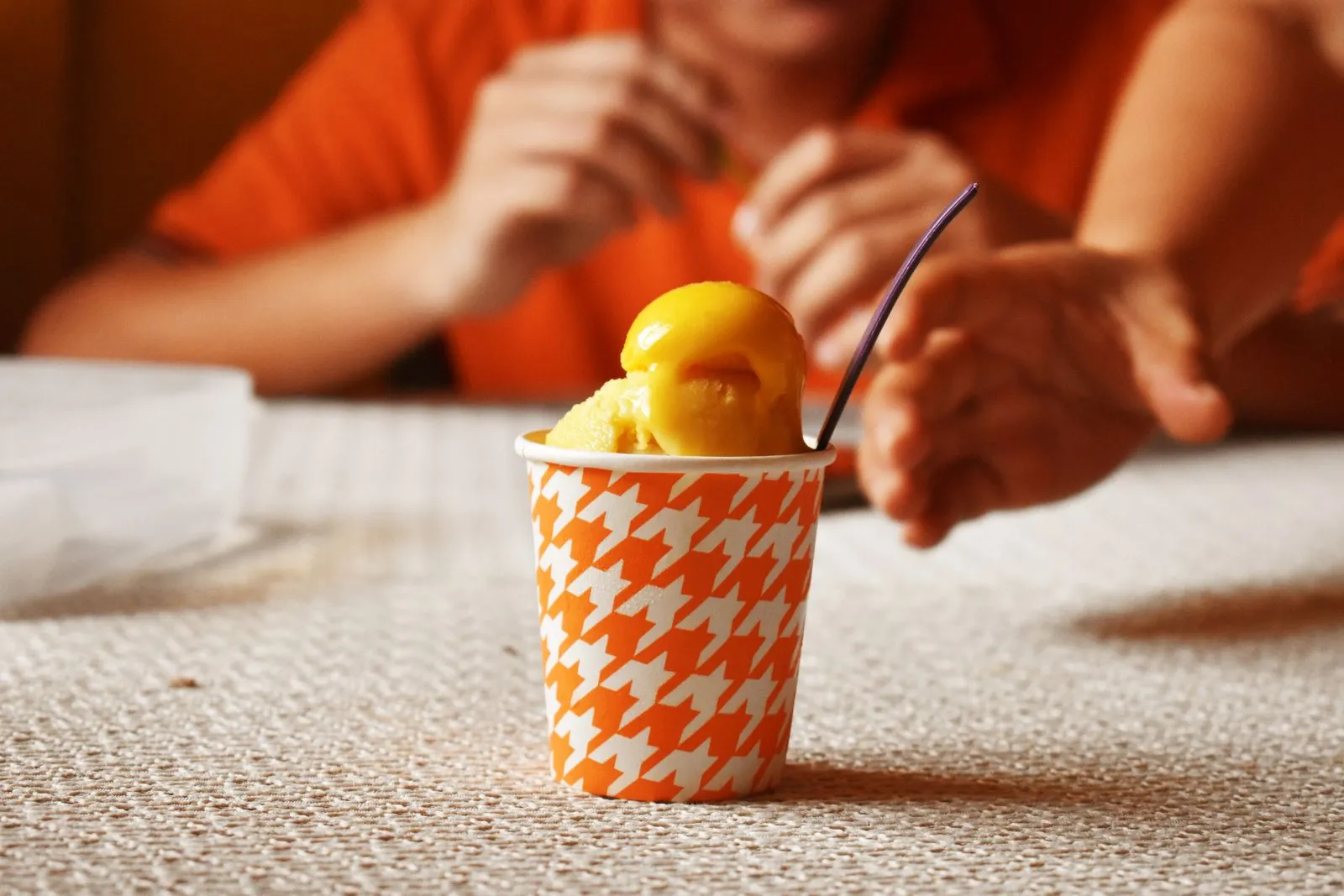 Delicious mango sorbet in an orange houndstooth cup with people reaching for it.